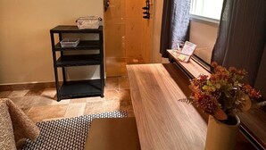 Ein gemütlicher Wohnraum mit einer Holzbank, einer kleinen Ablage mit Körben, einem Topfpflanzen und Blick auf eine Holztür, die nach draußen führt.