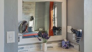 Un baño con un espejo grande, un televisor montado encima y una ventana con vistas a un globo aerostático.