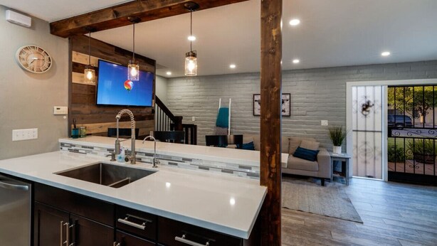 Una cocina moderna con una isla grande, vigas de madera, iluminación colgante y un televisor montado en la pared.
