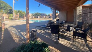 Un espacio al aire libre techado con piscina, sillas de descanso y una mesa.