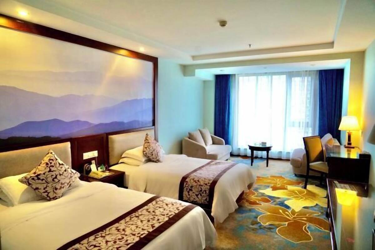 A hotel room with two beds, a desk, a chair, and a large window with curtains.