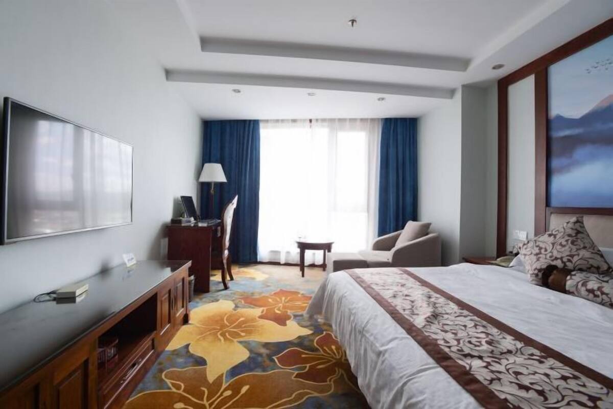 A hotel room with a bed, a TV, a desk, a chair, and a window with curtains.