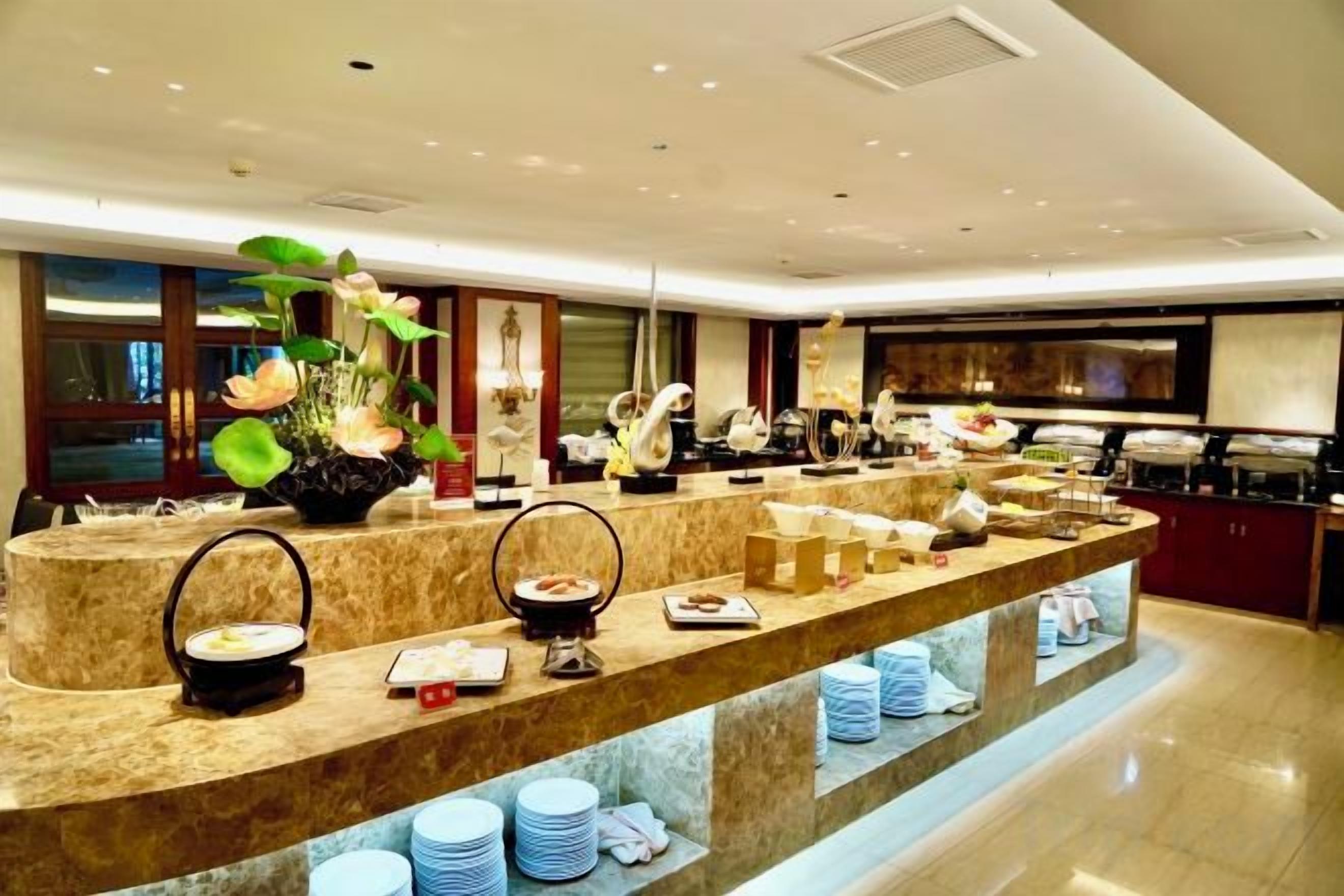 A buffet setup with multiple serving stations, a large vase with flowers, and a variety of dishes and utensils.