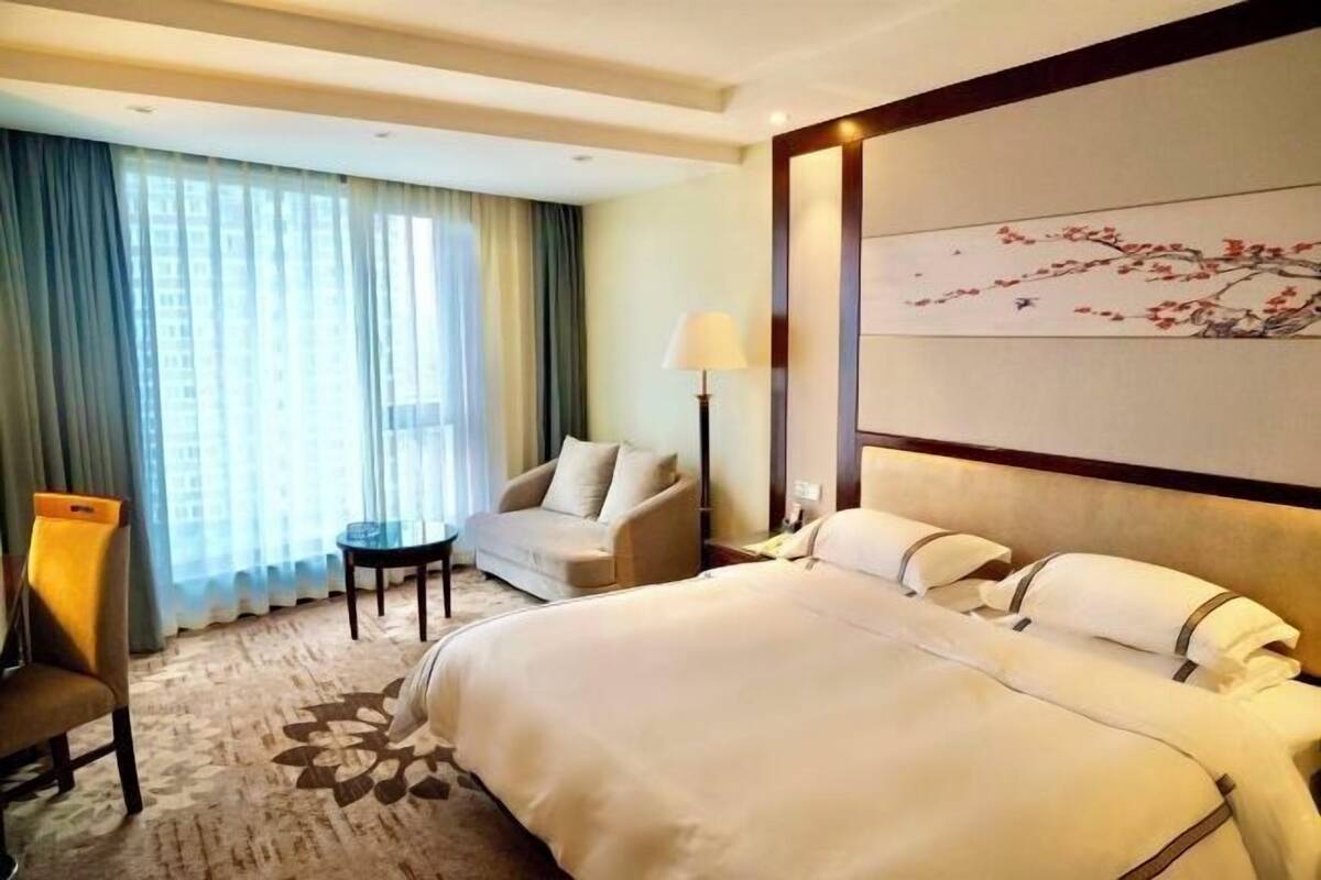 A hotel room with a large bed, a chair, a desk, and a lamp.