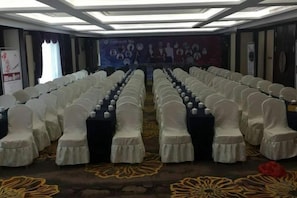 A conference room with rows of chairs and tables, a stage at the front, and a carpet with a floral pattern. - Xinxing Jingming Hotel (Ninghai)