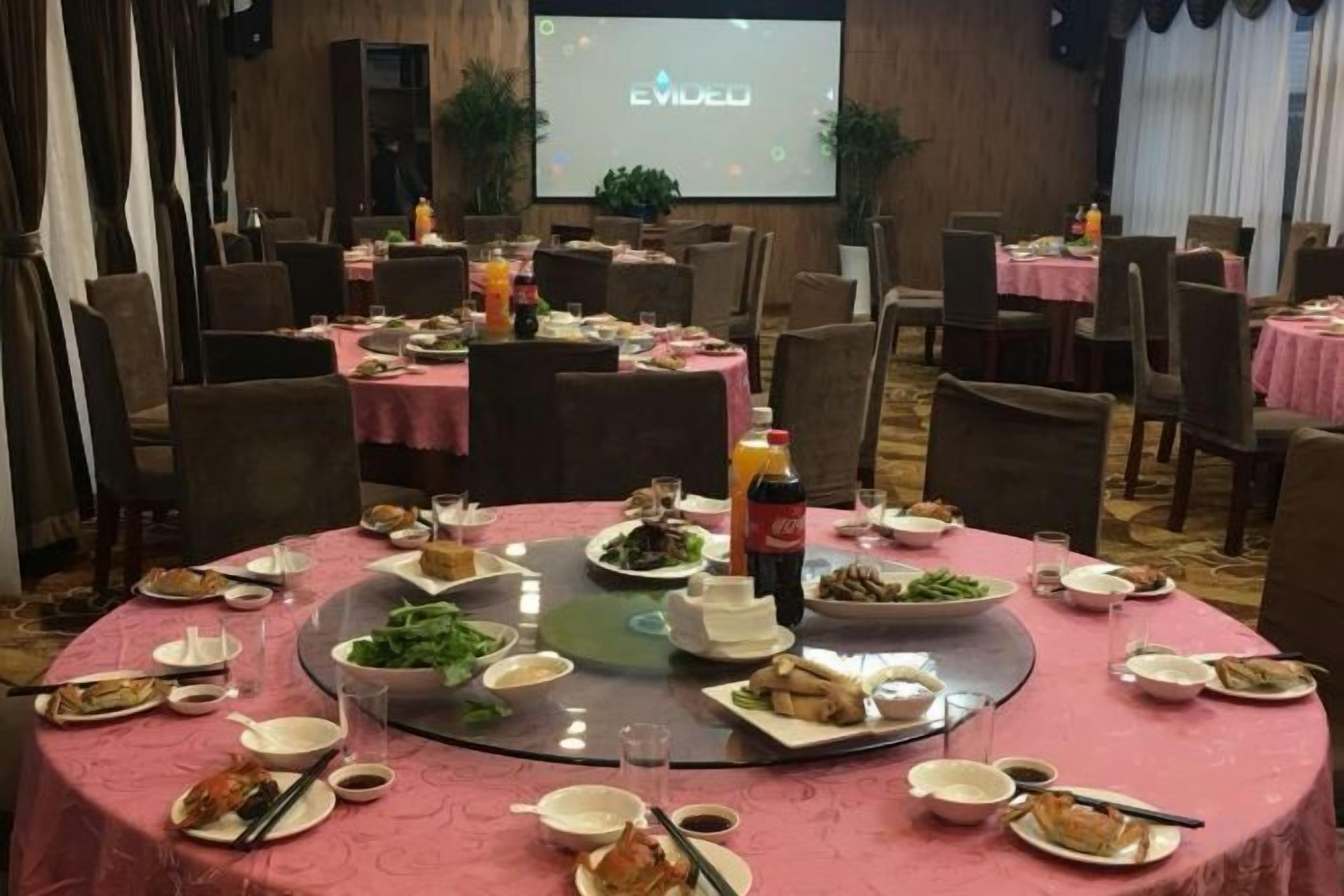 A conference room with round tables set for a meal, a projector screen in the background, and a presentation screen.