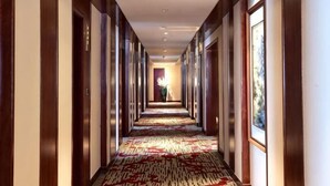 A hotel hallway with a patterned carpet, wooden doors, and framed artwork on the walls. - Xinxing Jingming Hotel (Ninghai)