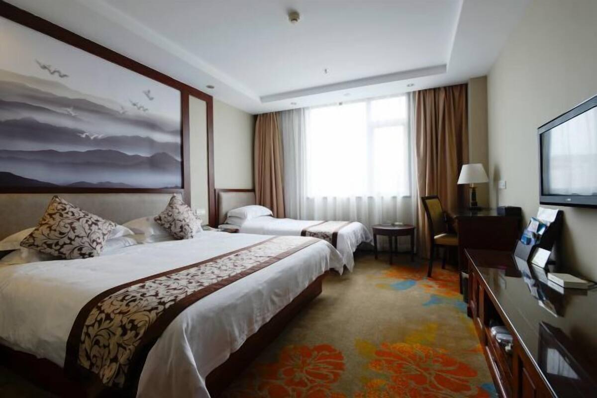 A hotel room with two beds, a desk, a chair, a TV, and a painting on the wall.