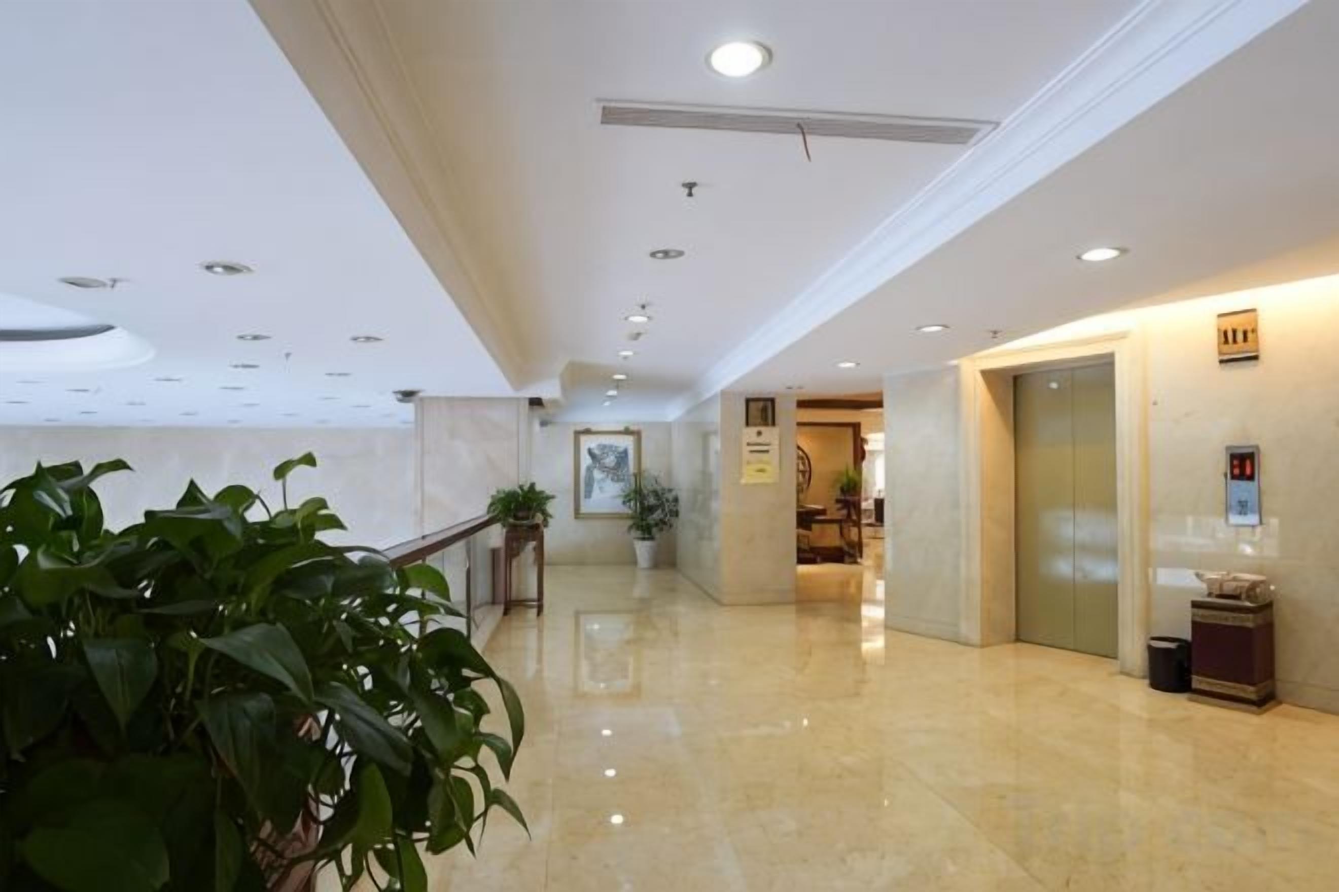 Un vestíbulo de hotel con piso pulido, una recepción, una planta en maceta y un ascensor.