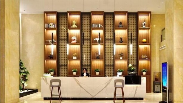 A reception desk with a marble counter, wooden shelving with decorative items, two bar stools, and a digital screen. - Xinxing Jingming Hotel (Ninghai)