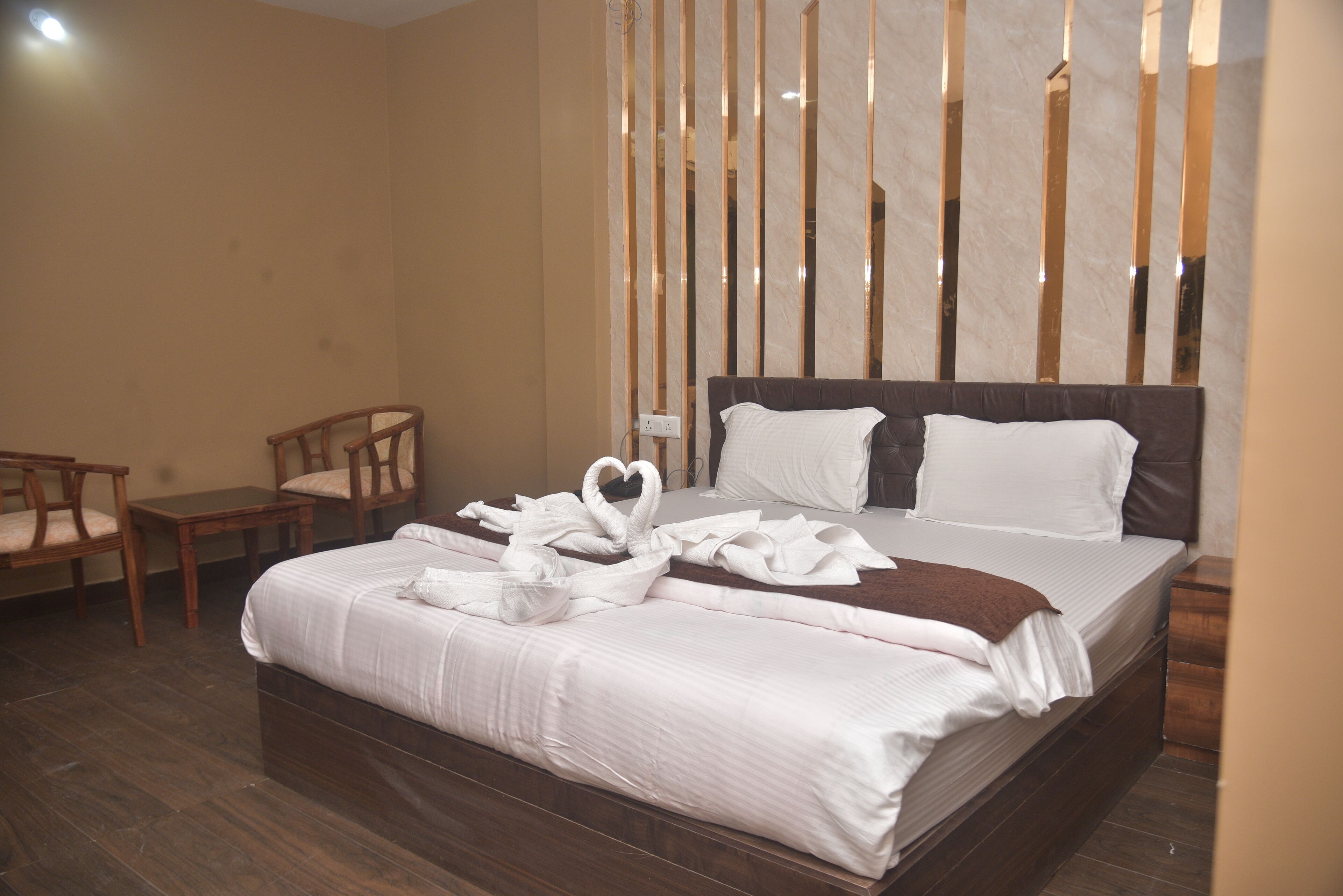 Una habitación de hotel con una cama grande, sillas de madera, una mesita pequeña y un panel decorativo en la pared.