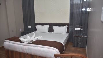 Een opgemaakt bed met witte lakens en een bruine plaid, een houten nachtkastje met een lamp, en een donker houten garderobe.