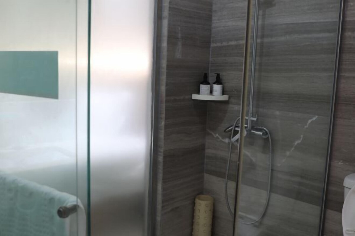 A glass-enclosed shower with a marble wall, a towel rack, and a shelf with toiletries.
