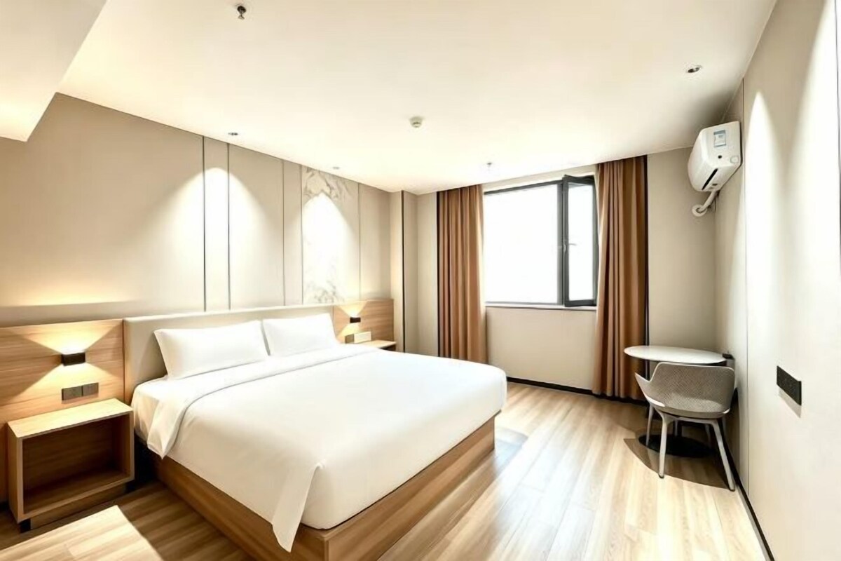 A modern hotel room with a large bed, bedside tables, a small desk, and a window with curtains.