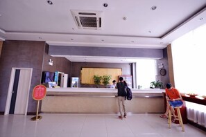 A reception area with a counter, a signboard, and a seating area with a plant. - Lejia Hotel (Bazhou Shengfang International Furniture Expo City) (Bazhou)