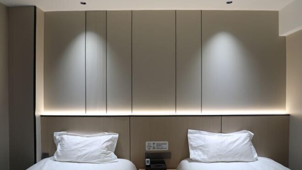 A modern hotel room with two beds, a bedside table, and a built-in headboard with integrated lighting. - Lejia Hotel (Bazhou Shengfang International Furniture Expo City) (Bazhou)