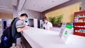 A reception desk with a counter, a plant, and a shelf with items. - Lejia Hotel (Bazhou Shengfang International Furniture Expo City) (Bazhou)