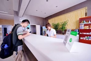 A reception desk with a counter, a plant, and a shelf with items. - Lejia Hotel (Bazhou Shengfang International Furniture Expo City) (Bazhou)