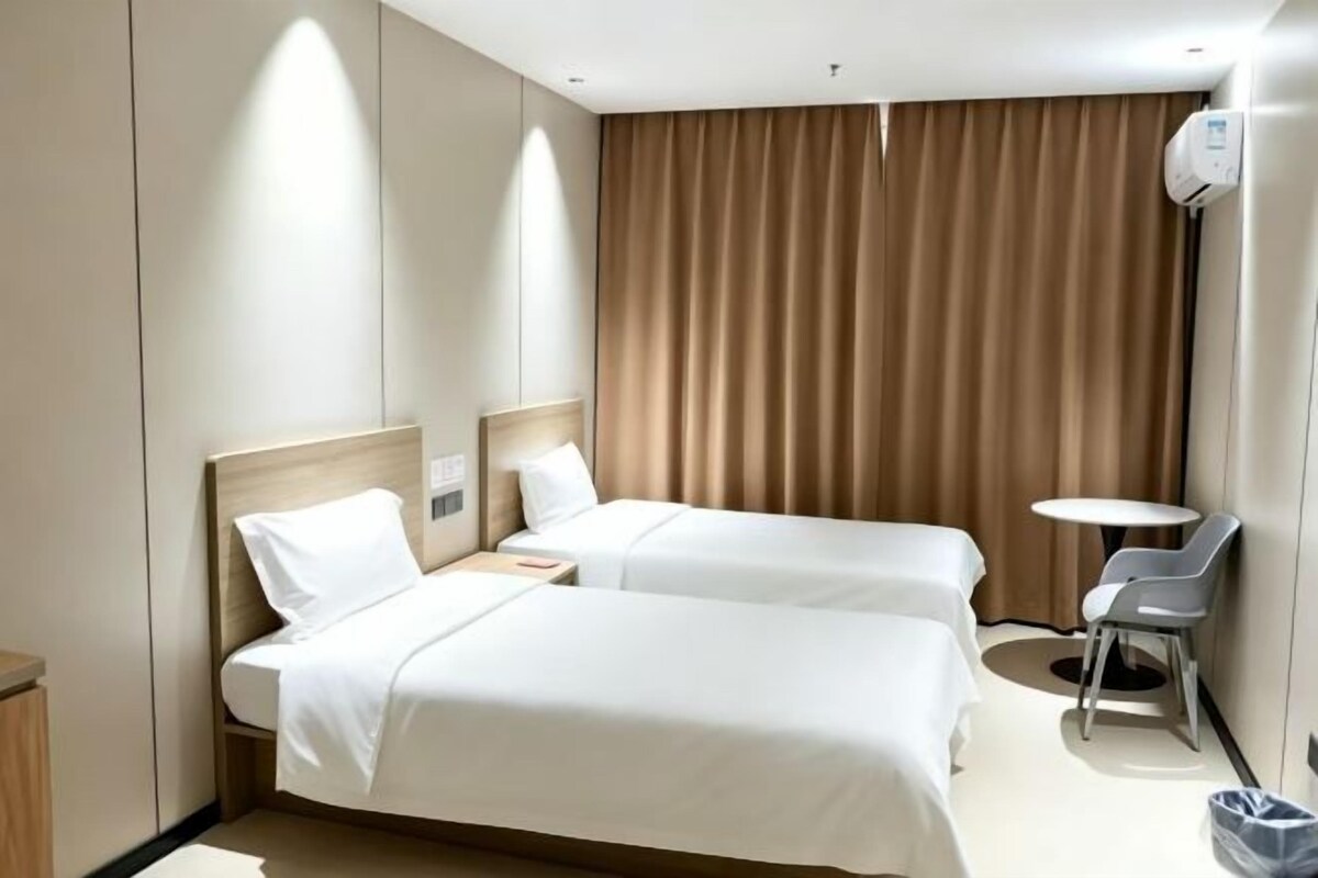 A hotel room with two beds, a small table, a chair, and a curtain.