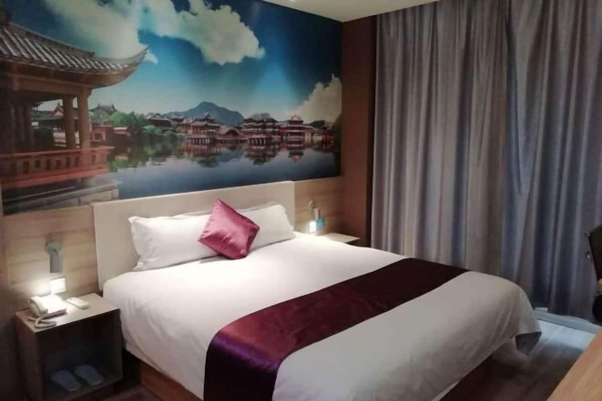 A hotel room with a large bed, a nightstand with a phone, and a painting of a traditional building on the wall.