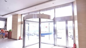 A revolving door with glass panels, a reception desk, and a view of parked cars outside. - Lejia Hotel (Bazhou Shengfang International Furniture Expo City) (Bazhou)