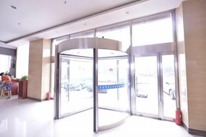 A revolving door with glass panels, a reception desk, and a view of parked cars outside. - Lejia Hotel (Bazhou Shengfang International Furniture Expo City) (Bazhou)