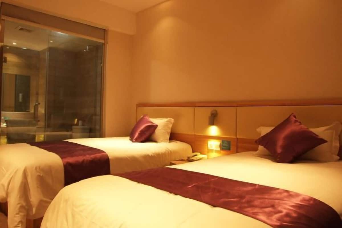 A hotel room with two beds, a glass shower enclosure, and a bedside table with a lamp.