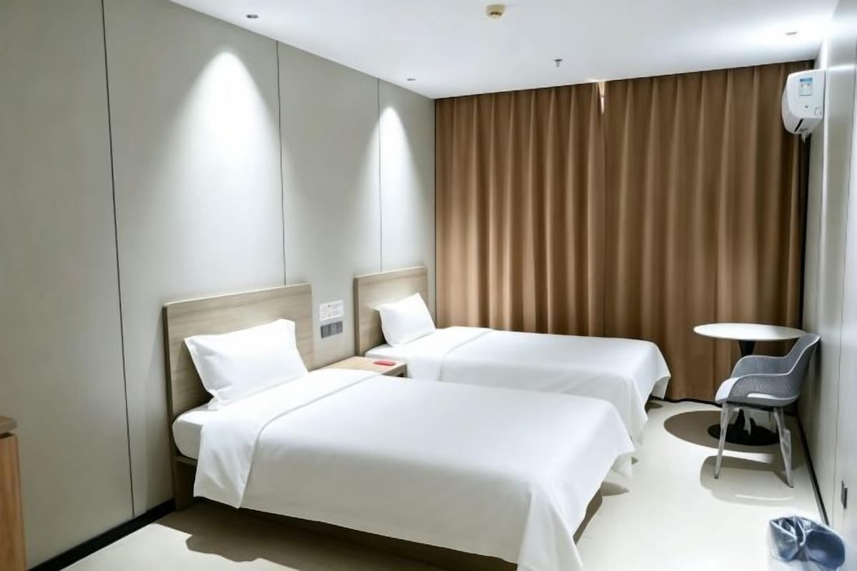Habitación de hotel con dos camas, una mesita, una silla y una cortina.