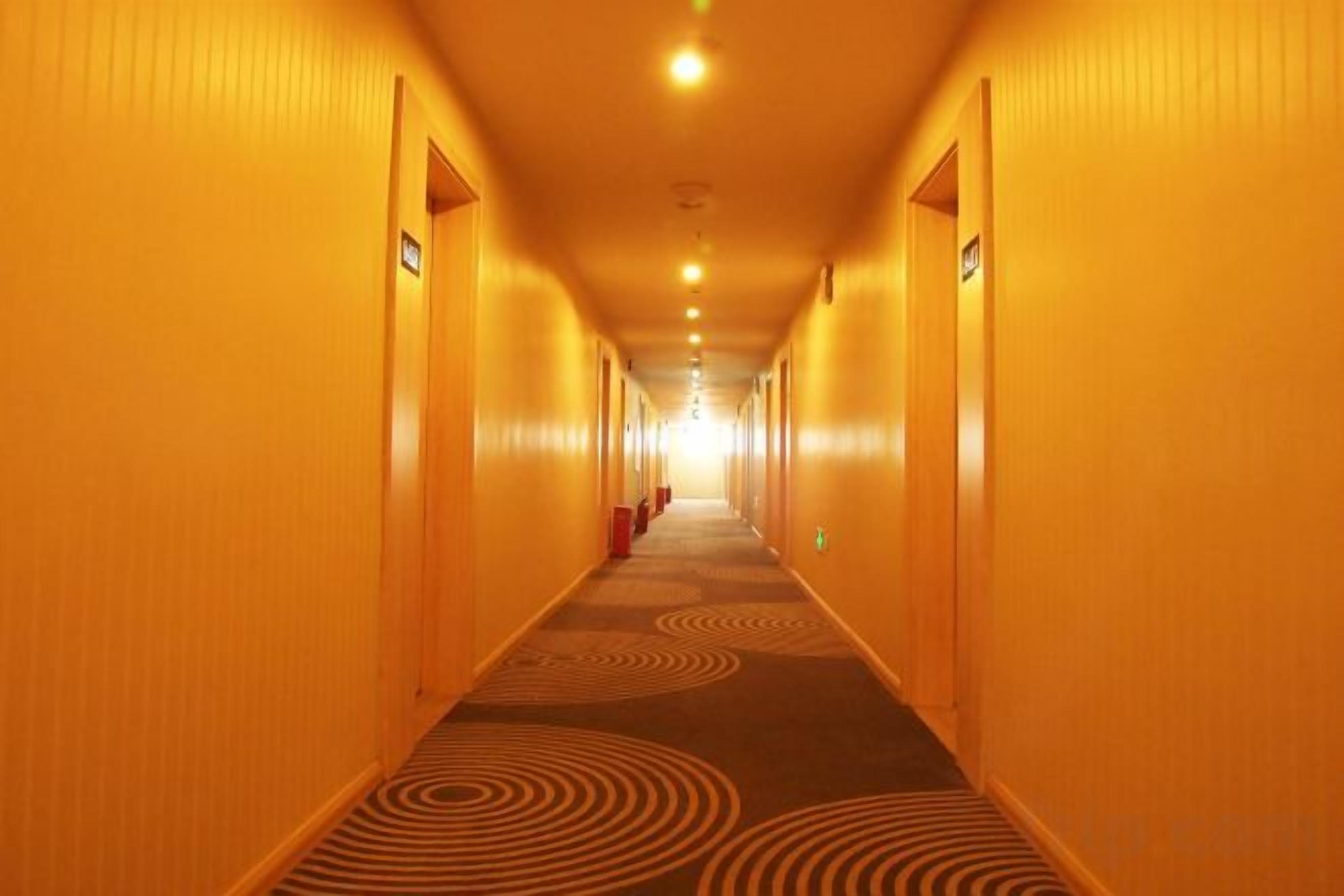 A hotel corridor with doors on both sides, a patterned carpet, and overhead lighting.
