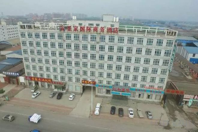 A multi-story building with a flat facade, several ground-level commercial spaces, and a parking lot with cars.