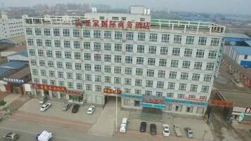 A multi-story building with a flat facade, several ground-level commercial spaces, and a parking lot with cars.