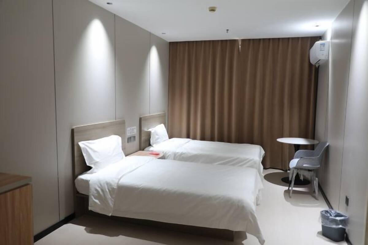 A hotel room with two beds, a small table, and a chair.