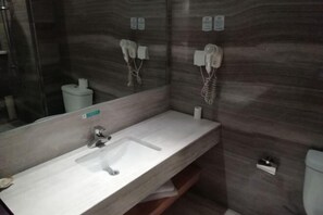 A modern bathroom with a white sink, a mirror, and a towel dispenser.