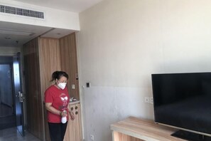 A room with a television, a wooden cabinet, and a person holding a white object. - Lejia Hotel (Bazhou Shengfang International Furniture Expo City) (Bazhou)