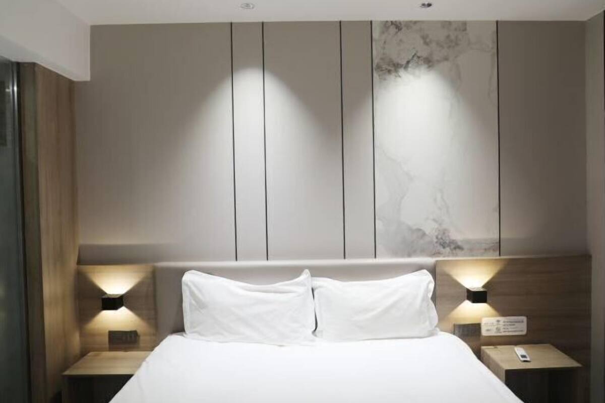 A modern hotel room with a large bed, two bedside tables with lamps, and a marble-patterned wall.
