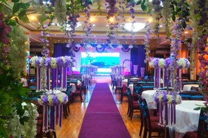 Un salón de banquetes con un pasillo central, mesas a ambos lados y un escenario al frente.