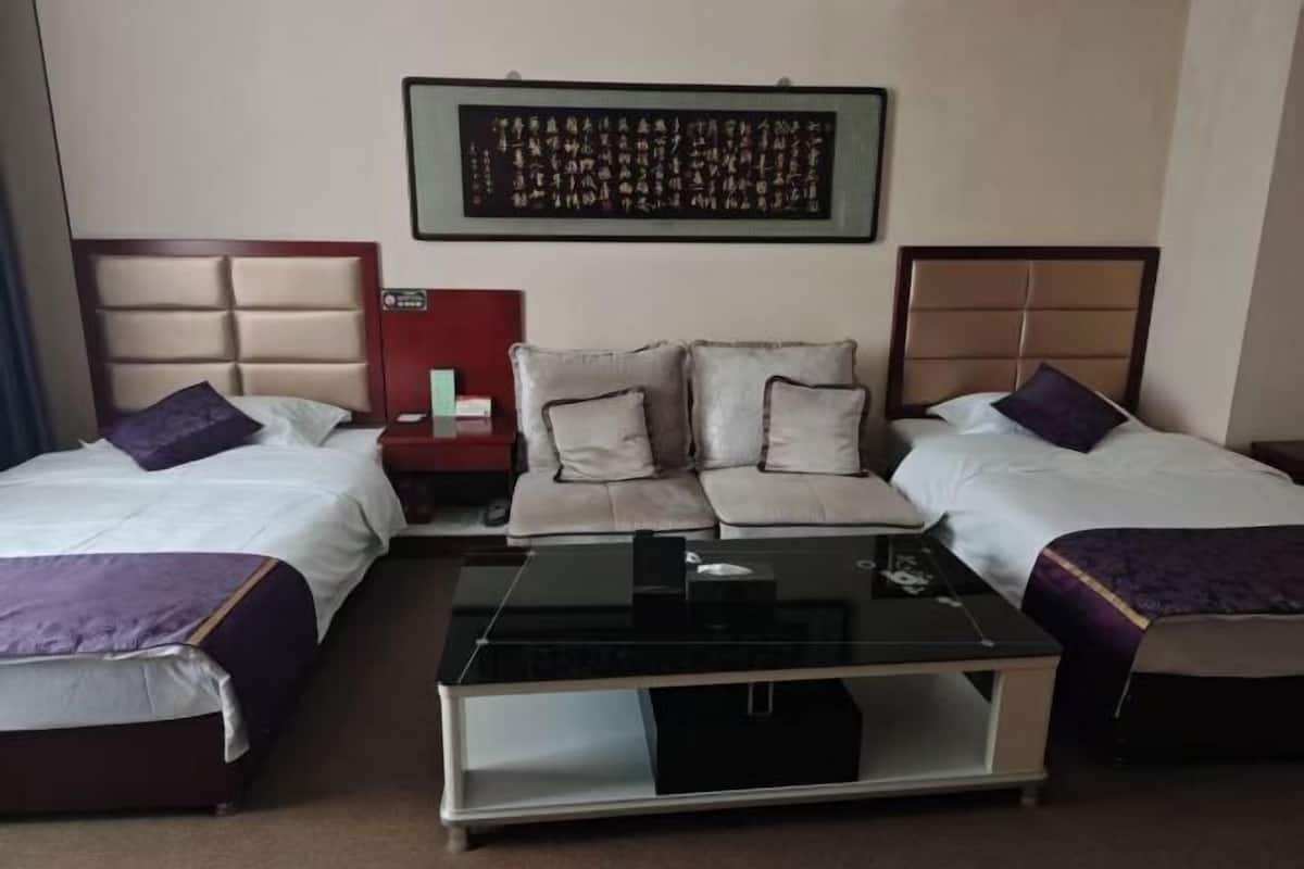 A hotel room with two beds, a sofa bed, a coffee table, a nightstand, and a wall art piece.