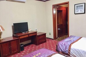 Una habitación de hotel con una cama, un escritorio con televisor, una silla y una puerta que da a otra habitación.