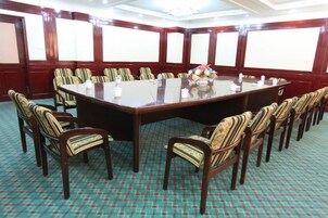 Una sala de conferencias con una gran mesa rectangular rodeada de sillas, suelo alfombrado y una pizarra en la pared.