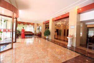 Un vestíbulo de hotel con piso de mármol, una recepción y una gran planta en maceta.