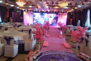 Un salón de banquetes con filas de mesas redondas, un escenario con una pantalla grande y centros de mesa florales.