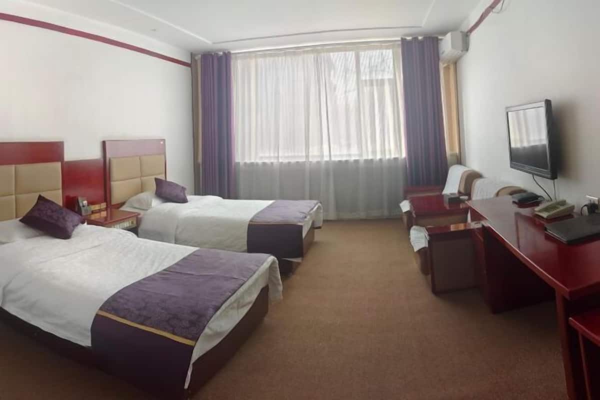 A hotel room with two beds, a desk, a television, and a window with curtains.