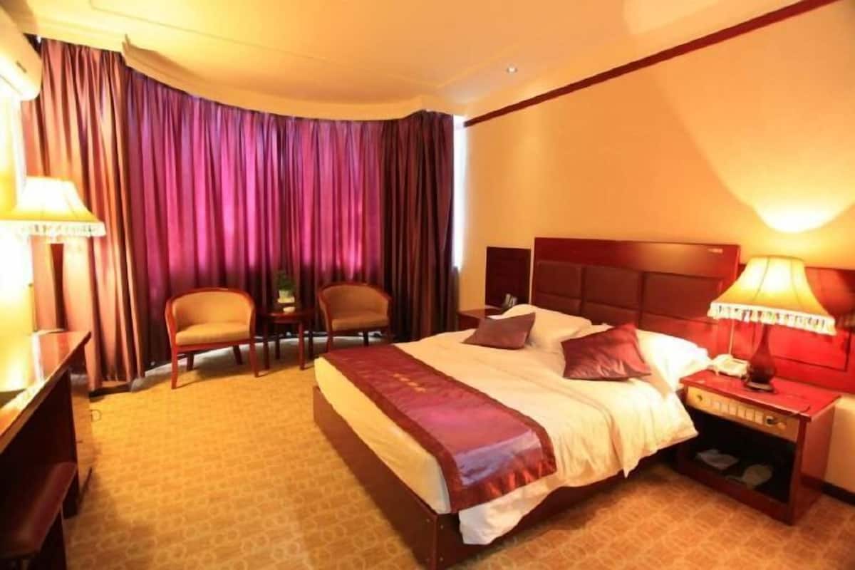 A hotel room with a bed, two chairs, a nightstand, and a lamp.