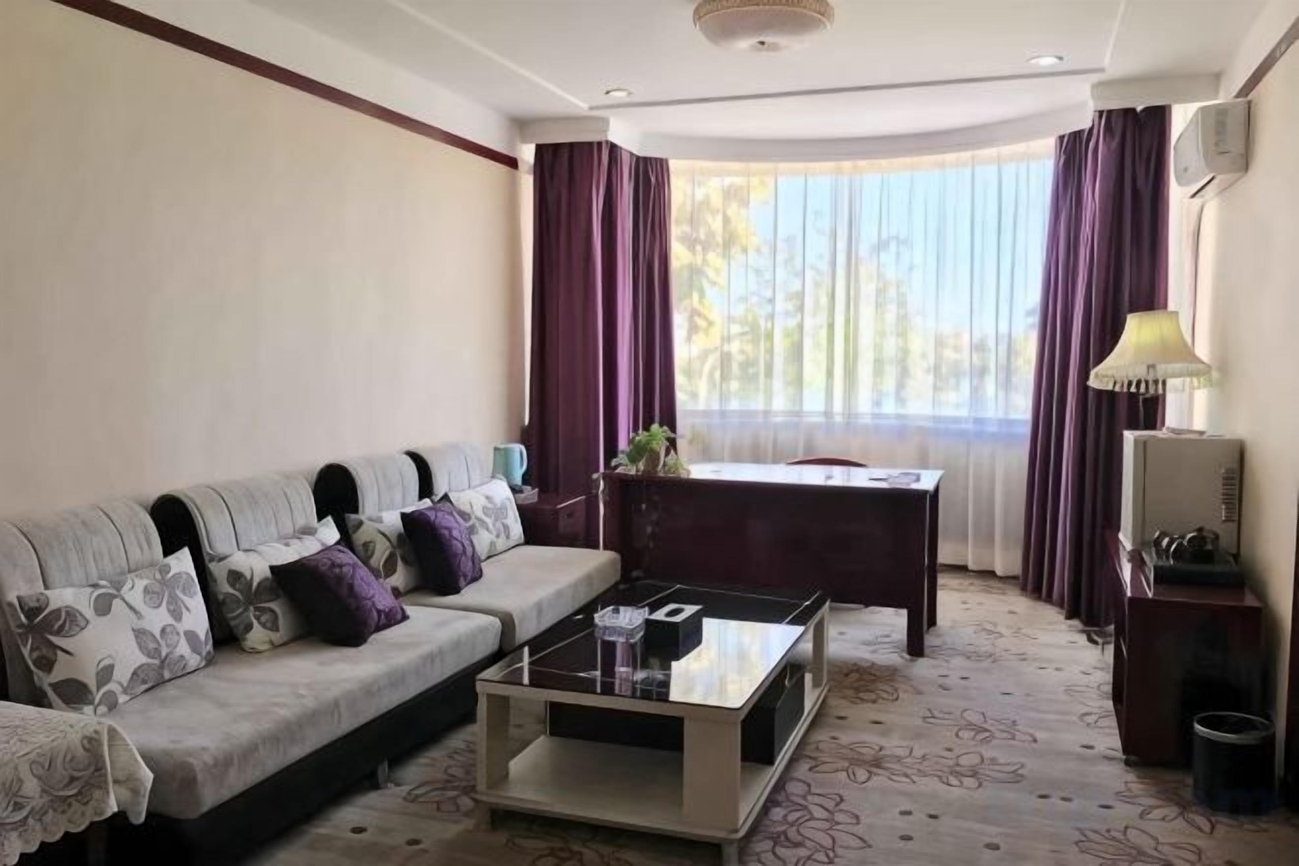 A hotel room with a sofa, a coffee table, a desk, and a lamp.