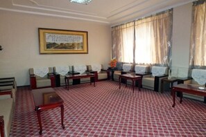 A hotel room with a red patterned carpet, a sofa set, a coffee table, and a framed picture on the wall. - Jinta Hotel (Jinta)