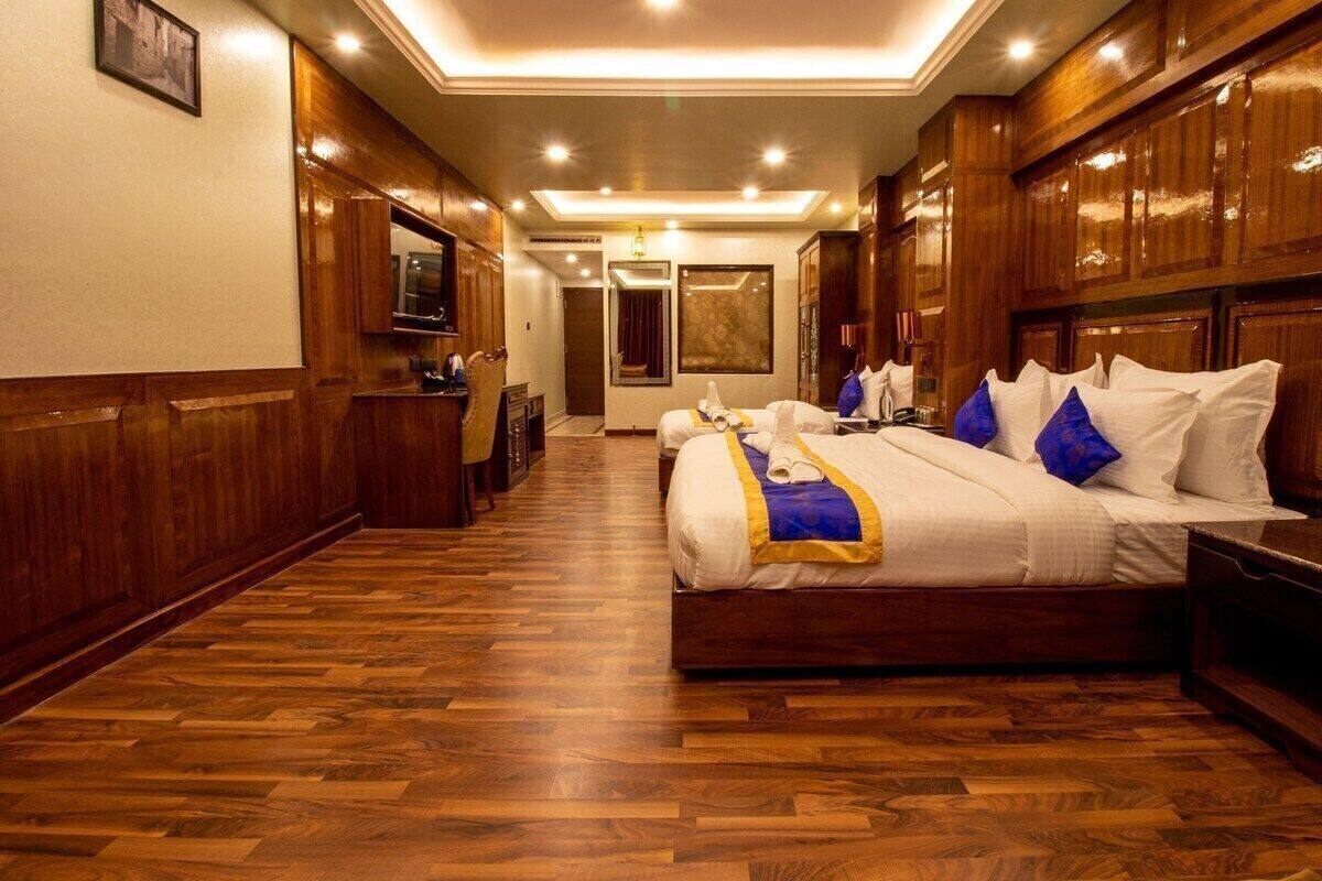 Habitación de hotel con piso de madera, una cama grande con ropa de cama blanca y detalles azules, un escritorio con una silla y un televisor en la pared.