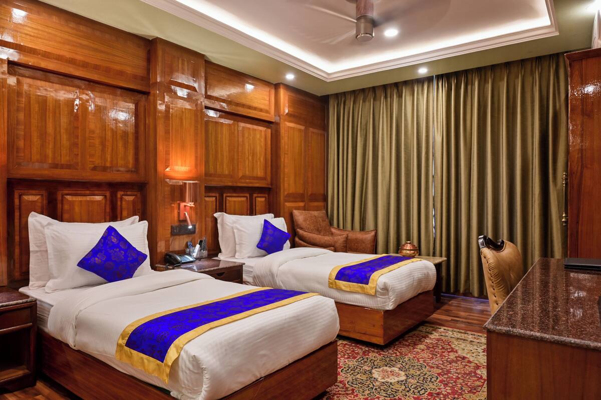 Habitación de hotel con dos camas, paneles de madera, un escritorio y un ventanal con cortinas.