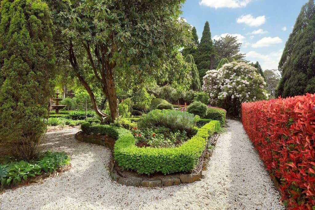 A garden with a gravel path, neatly trimmed hedges, and various trees.