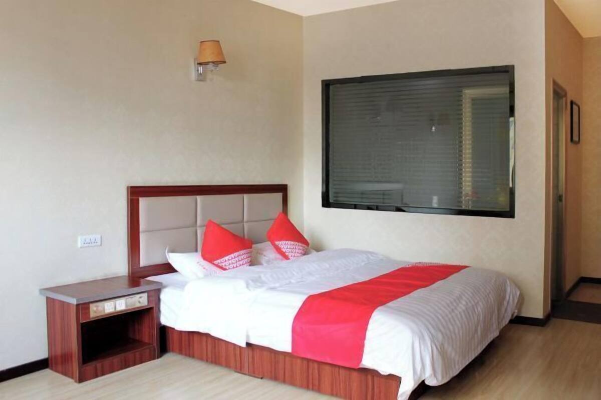 A hotel room with a bed, a nightstand, a lamp, and a window.