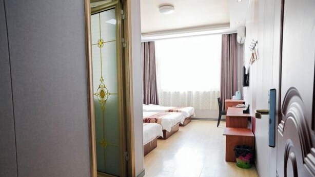 A hotel room with a bed, a desk, a chair, a small table, a trash bin, and a door. - Taidawenquanbinguan (Yongqing)
